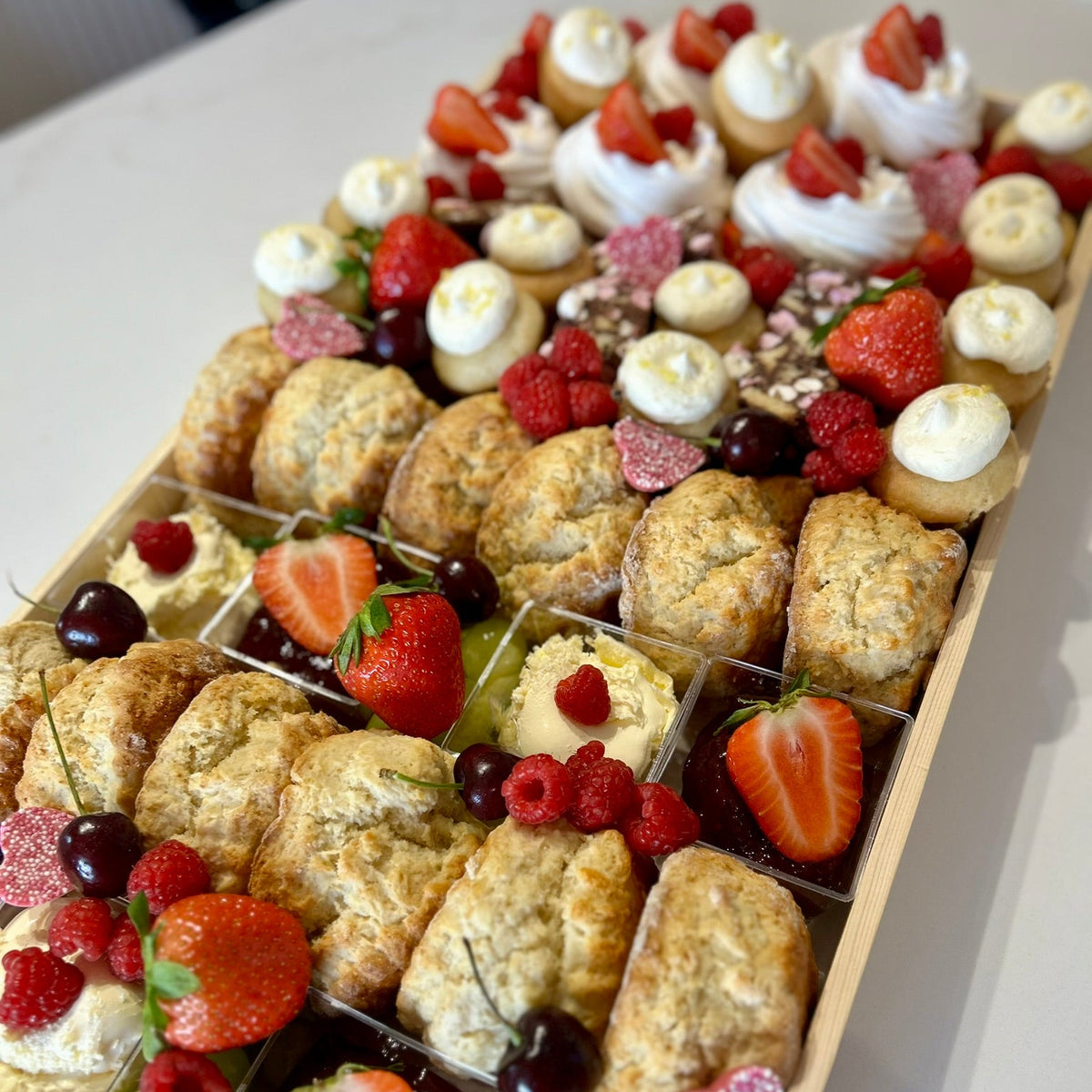 Assorted cakes, scones and fruits in a wooden box on a white surface