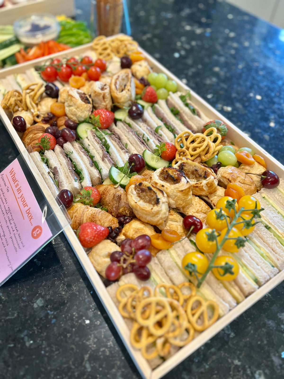 Assorted finger food platter with sandwiches, fruits, and snacks on a black countertop.