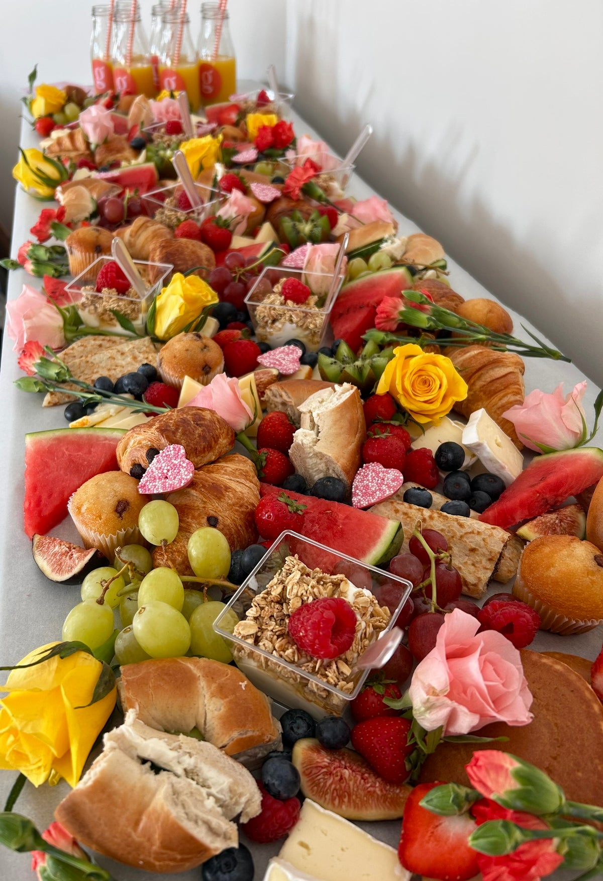 Dessert table with various pastries, fruits, and flowers on a white surface.