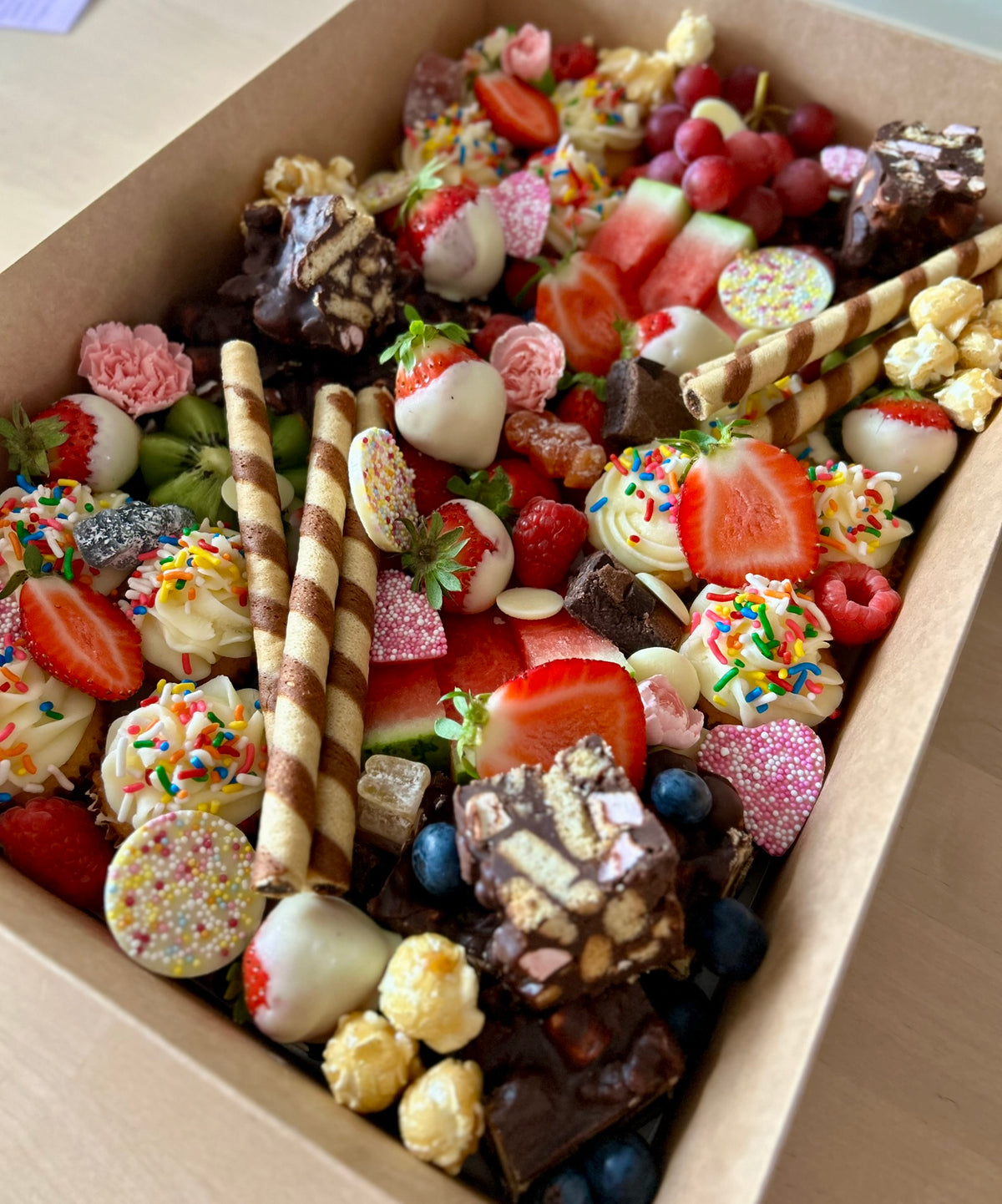 Assorted candy and fruit in a box on a wooden surface