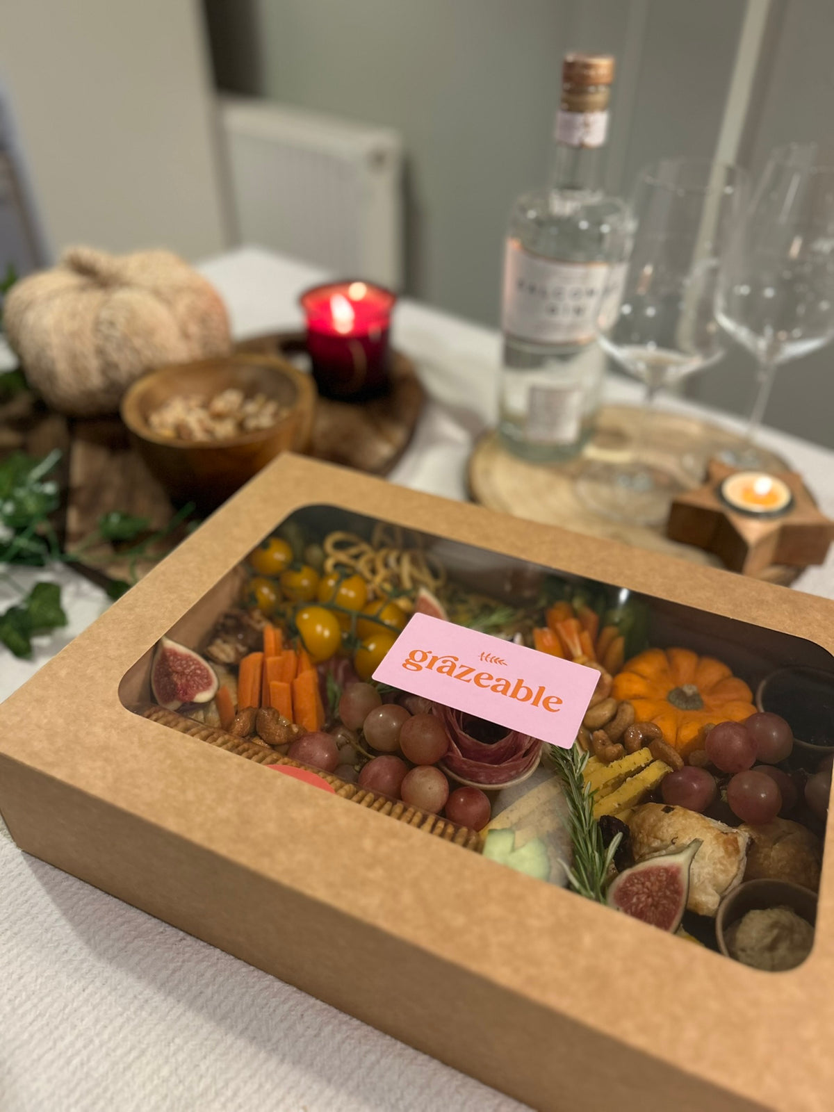 Grazeable box with assorted snacks on a table with a bottle of gin and glasses.