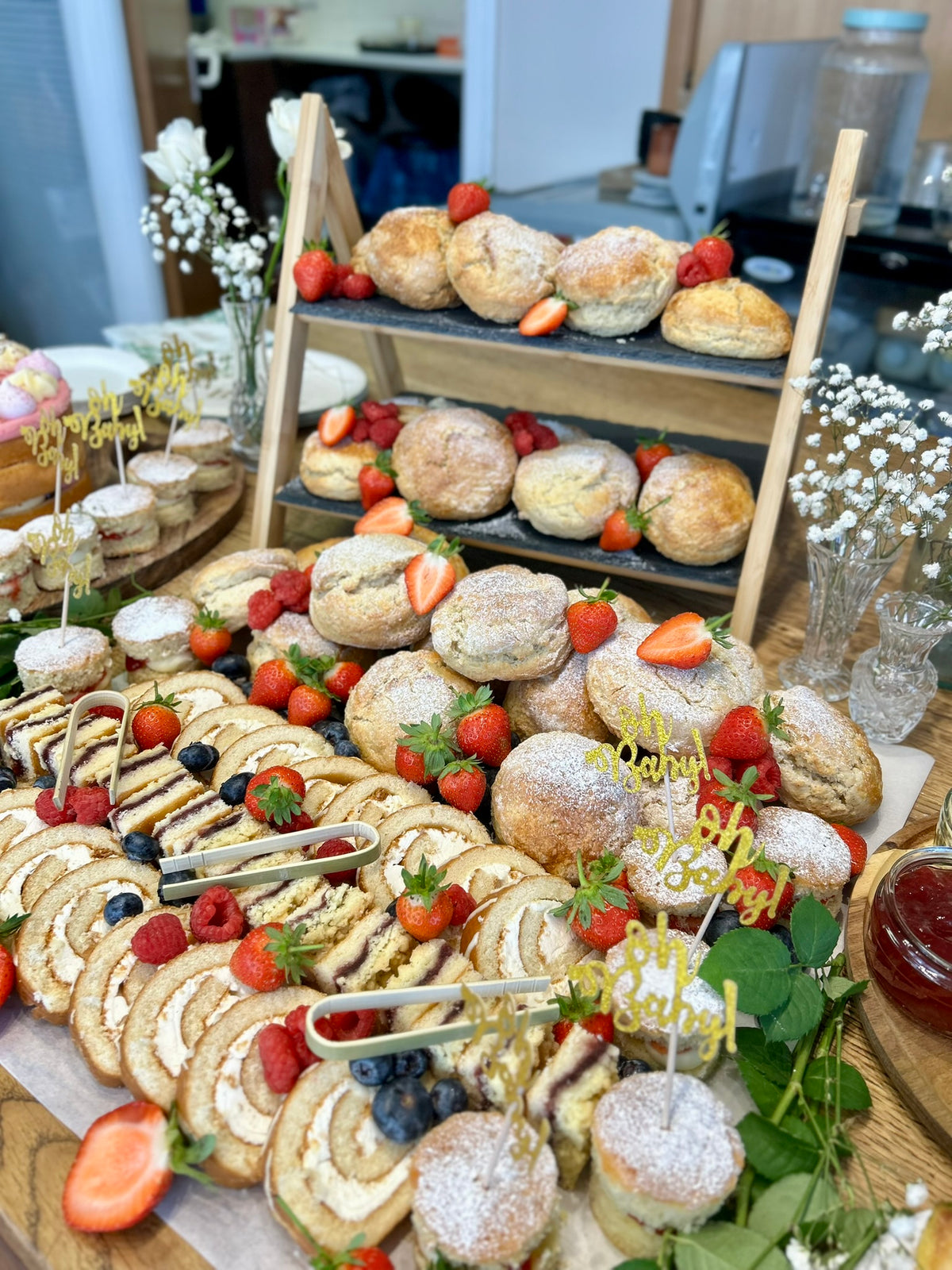 Afternoon tea table with scones, cakes, fruits, and flowers in a cafe setting