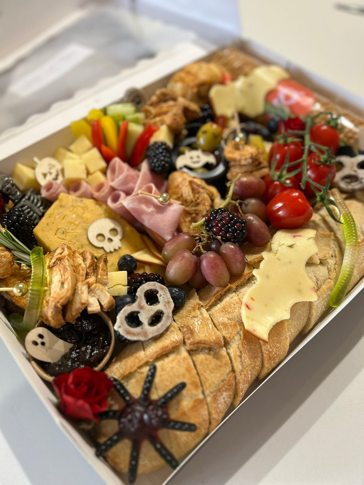 Assorted charcuterie box with bread, meats, and vegetables on a white surface
