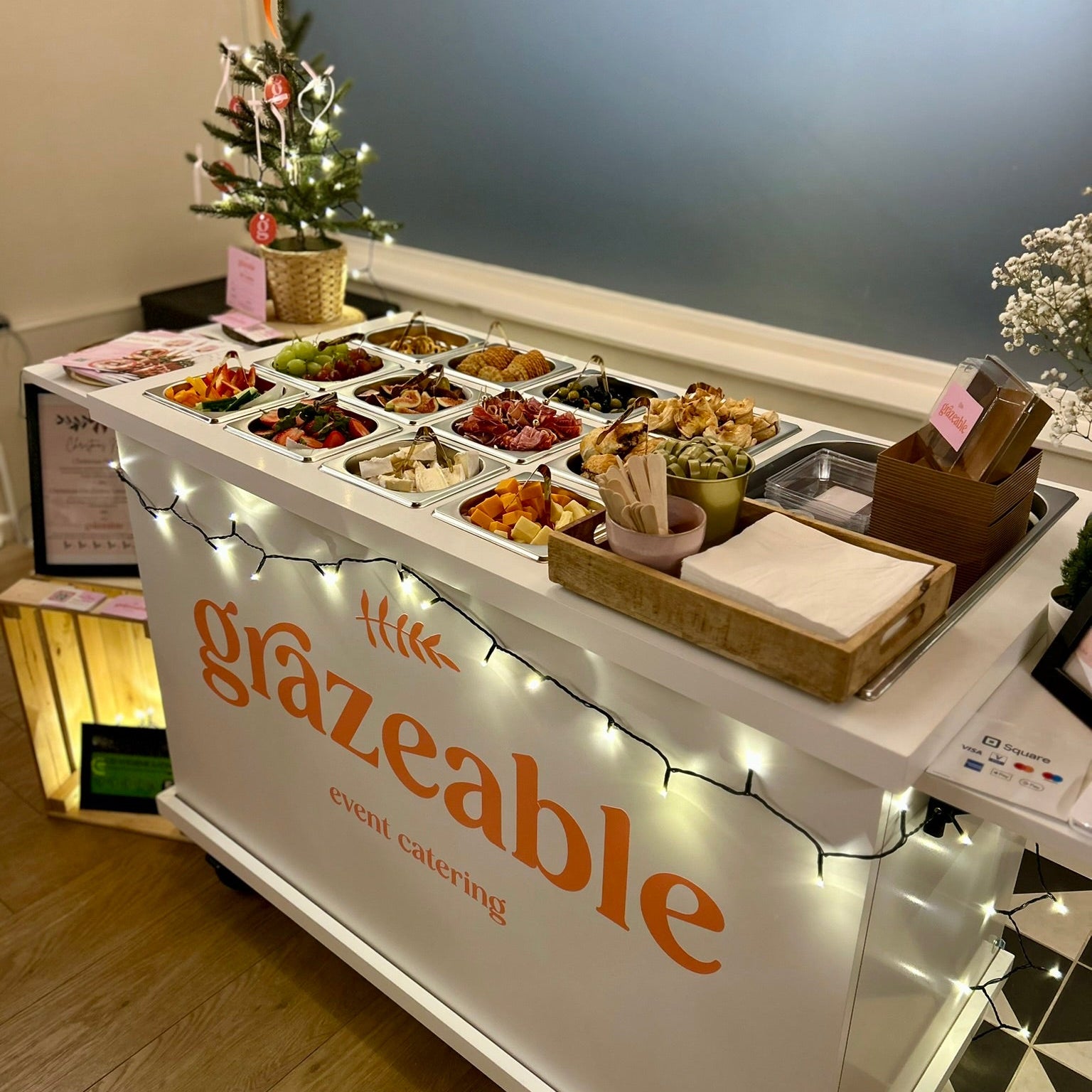 Grazeable event catering station with various food options and decorative lights.