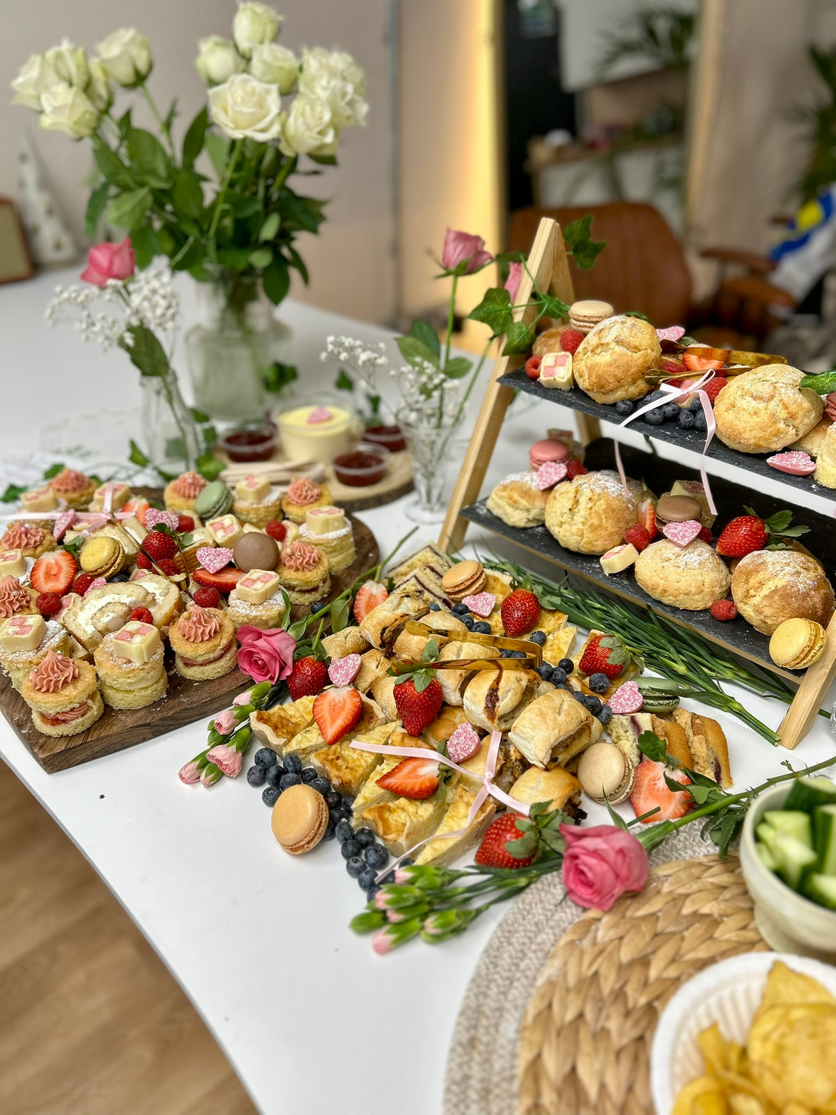 Table with various pastries, flowers, and a candle in a blurred indoor setting