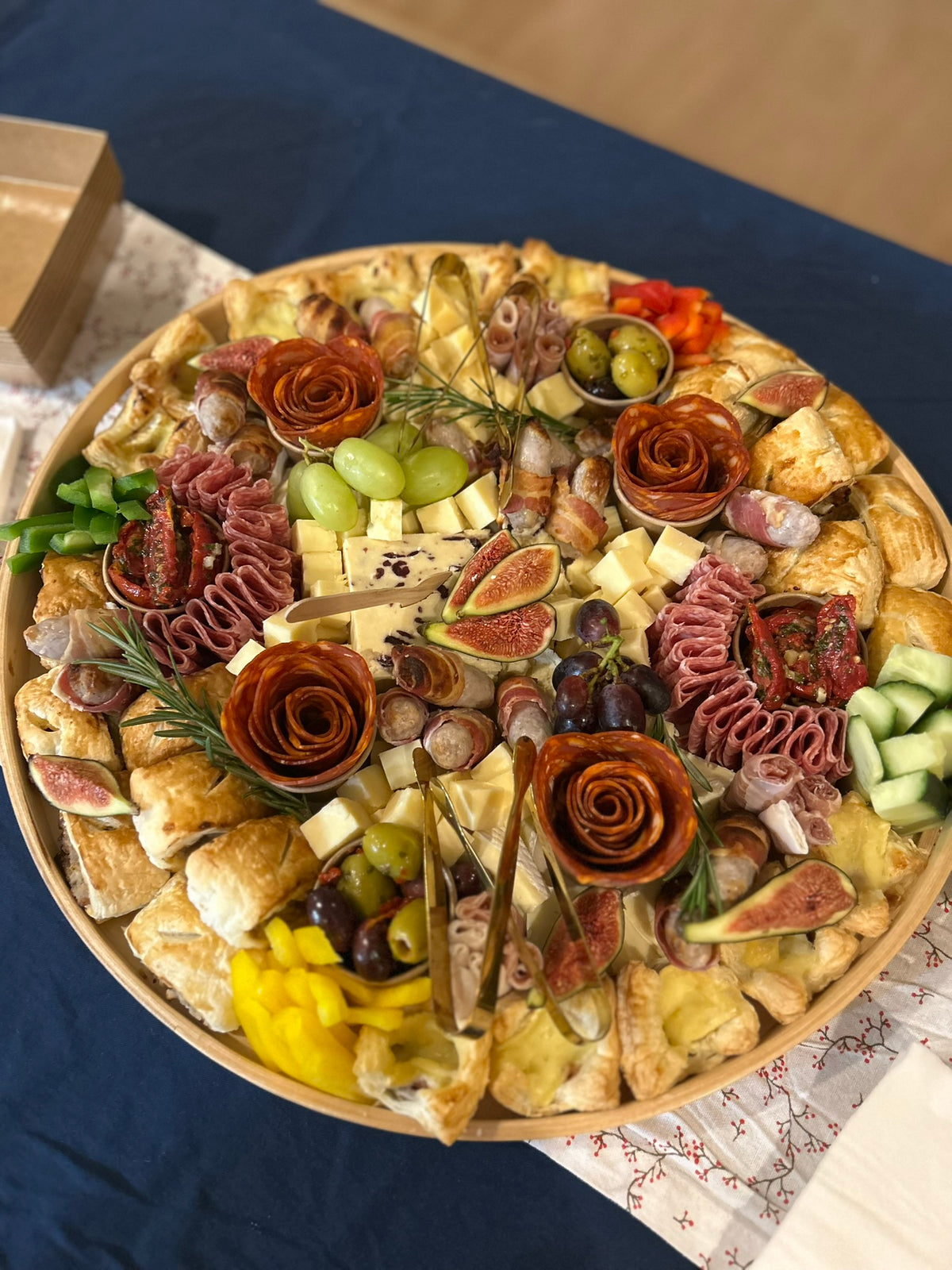 Decorative platter with assorted meats, cheeses, and fruits on a blue tablecloth.