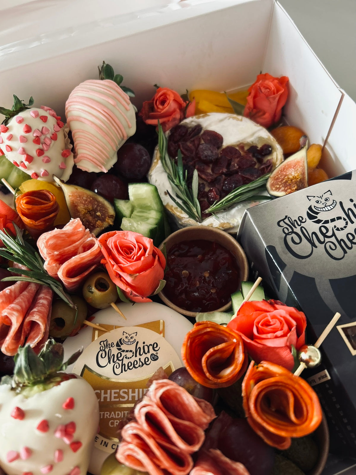 Assorted food items including meats, cheeses, and fruits in a decorative box with 'The Cheshire Cheese' branding.
