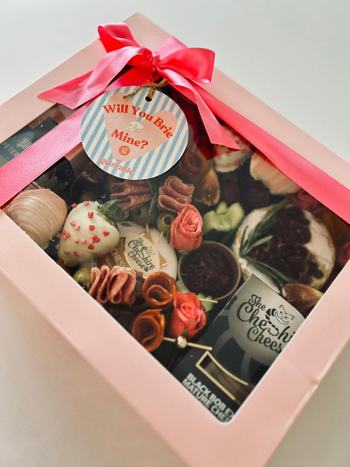 Box of assorted savoury food with chocolate covered strawberries  with a pink ribbon and 'Will You Brie Mine?' tag.