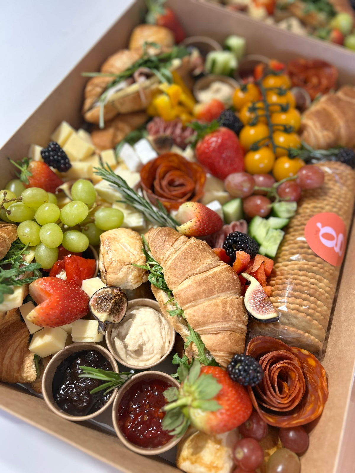 Assorted savoury grazeable with fruits, bread, and condiments in a box.