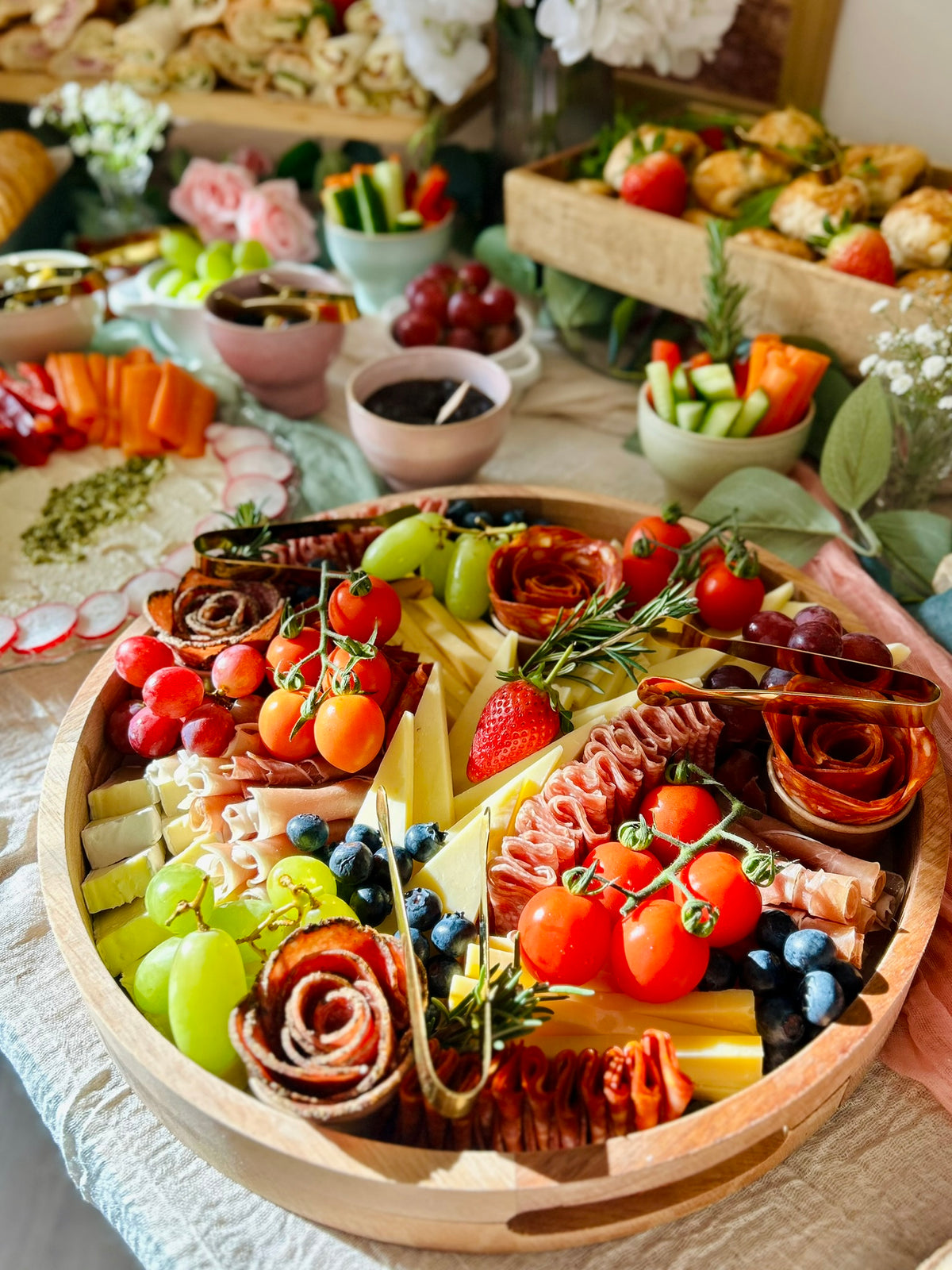 Assorted charcuterie board with fruits, vegetables, and meats on a wooden platter.