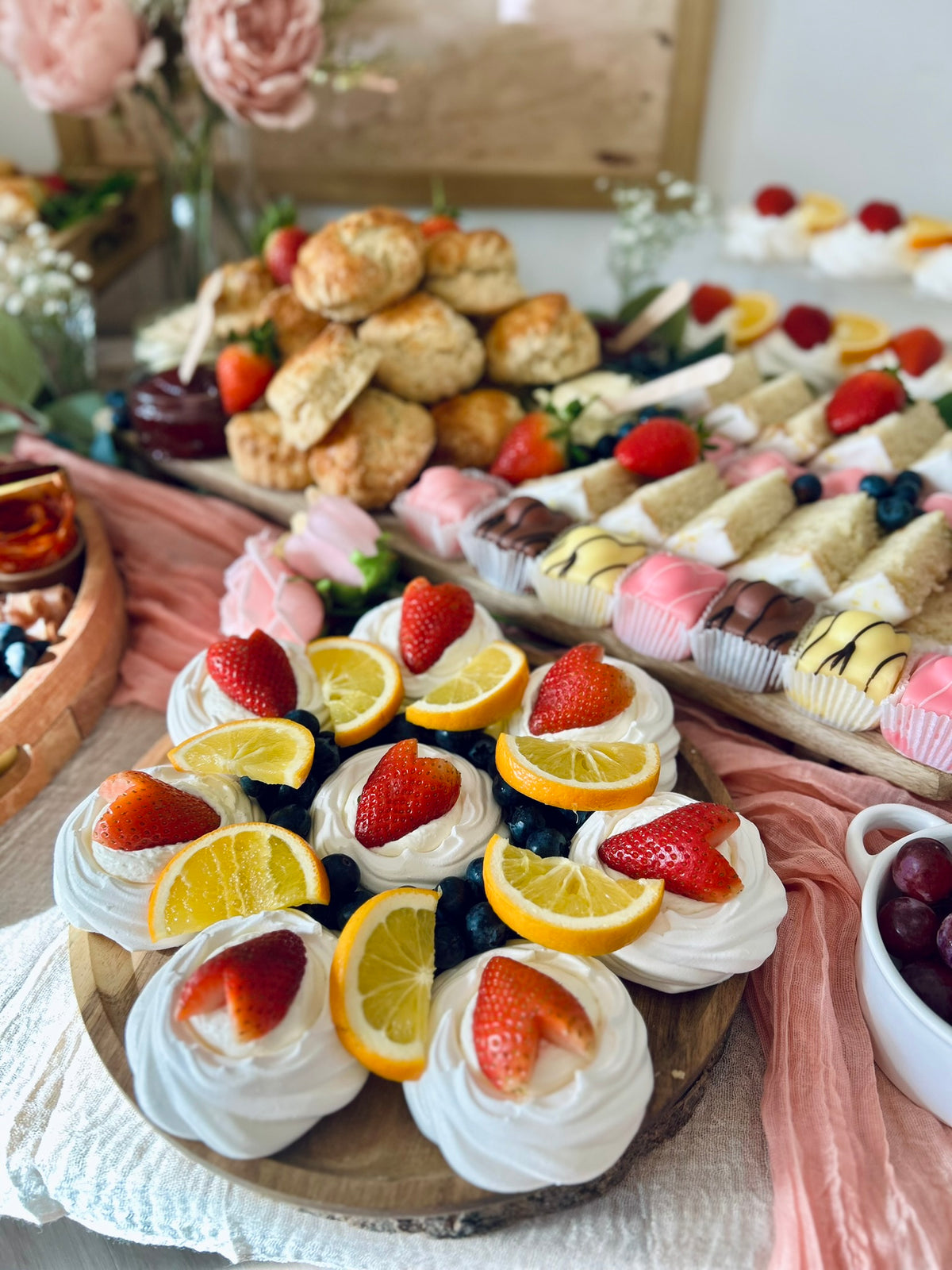 Assorted desserts including cakes, meringues and fruits on a wooden board.