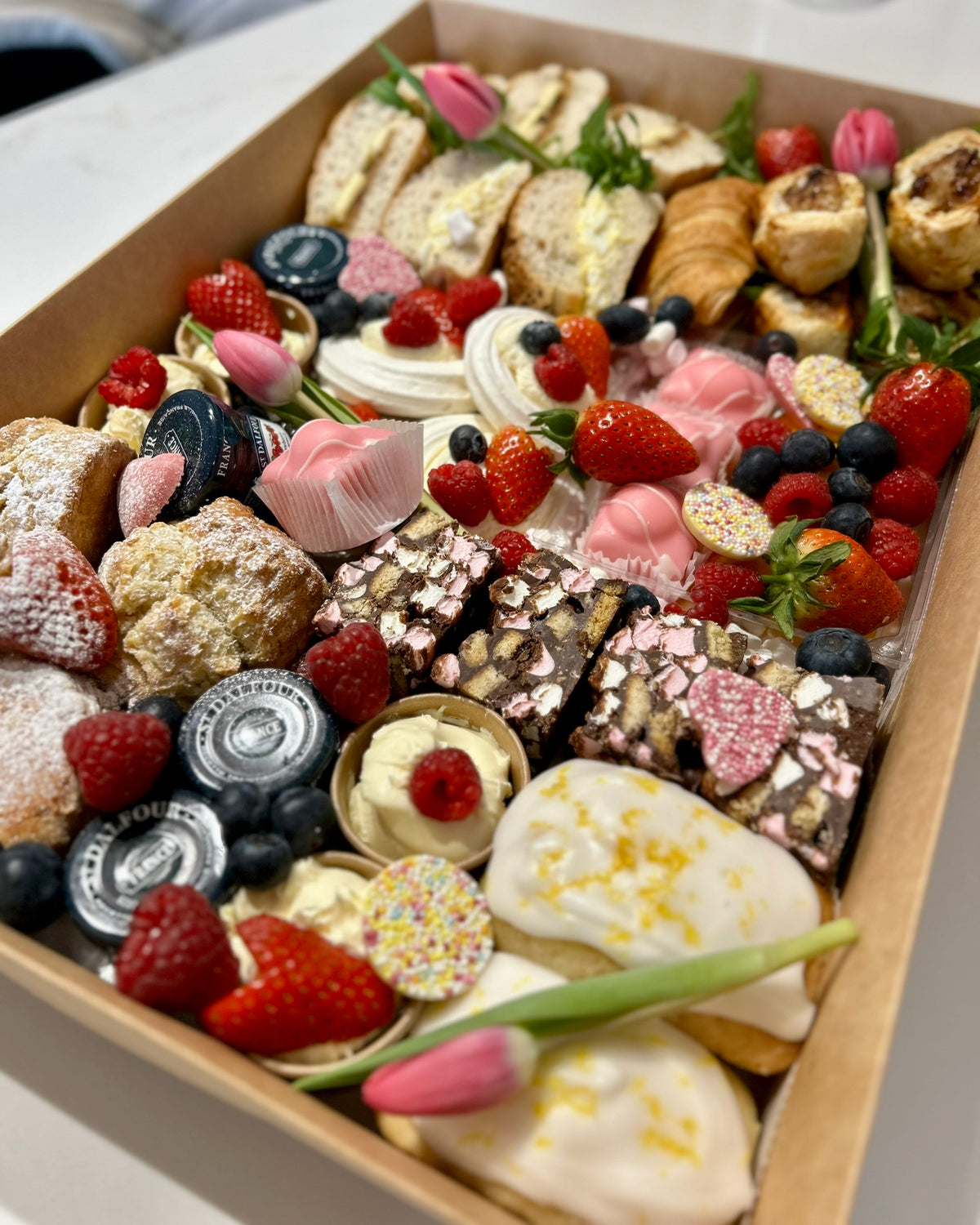 Afternoon tea grazeable box with assorted pastries and desserts with berries and flowers.