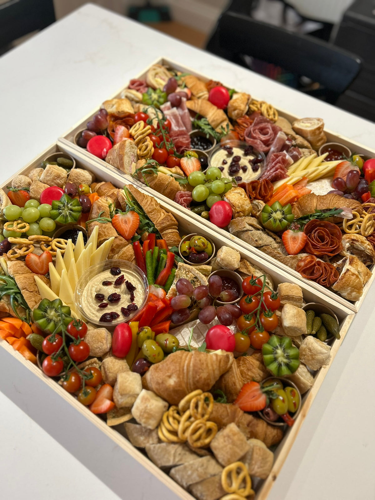 Two wooden charcuterie boards filled with an assortment of meats, cheeses, fruits, and vegetables on a white surface.
